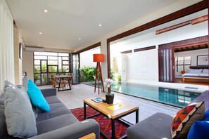A modern living room with a pool view, grey sofas, a wooden coffee table, and a red lamp.