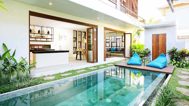 A modern house with a swimming pool, a balcony, and a kitchen visible through an open door.