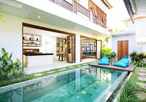 A modern house with a swimming pool, a balcony, and a kitchen visible through an open door.