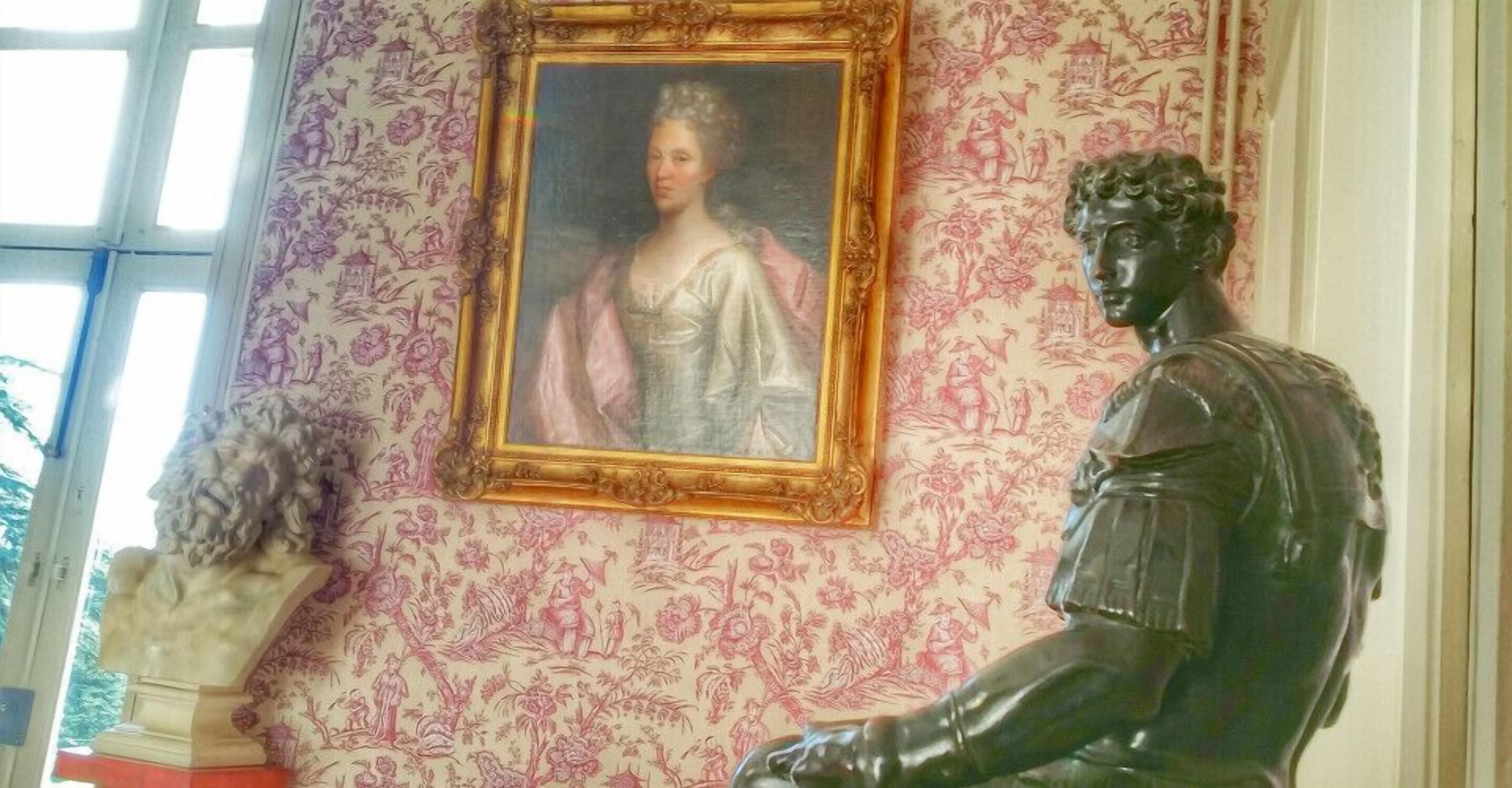 A room with a statue, a framed portrait, and patterned wallpaper.