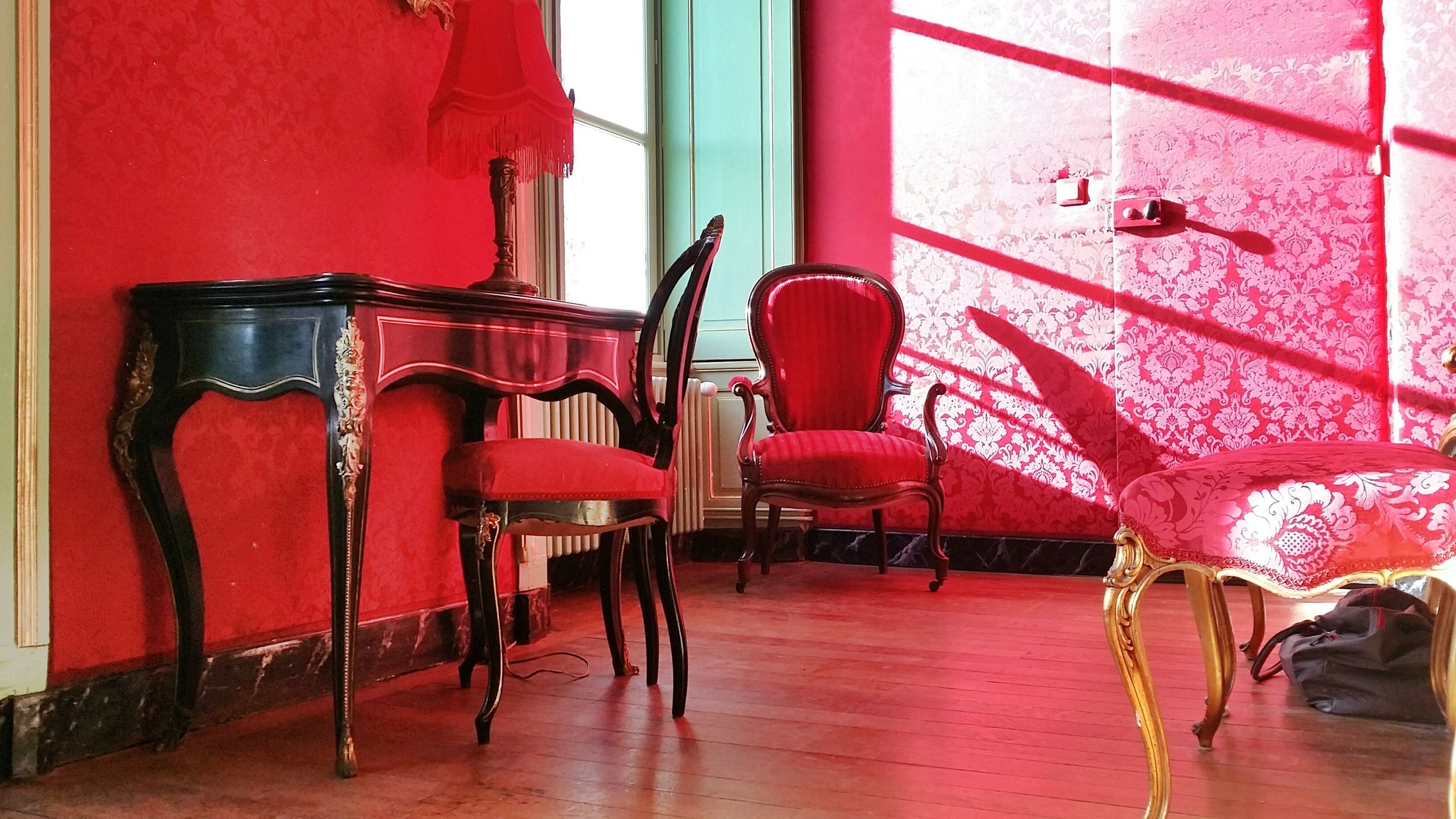 Una habitación con pared roja, un escritorio de madera, dos sillas y un radiador.