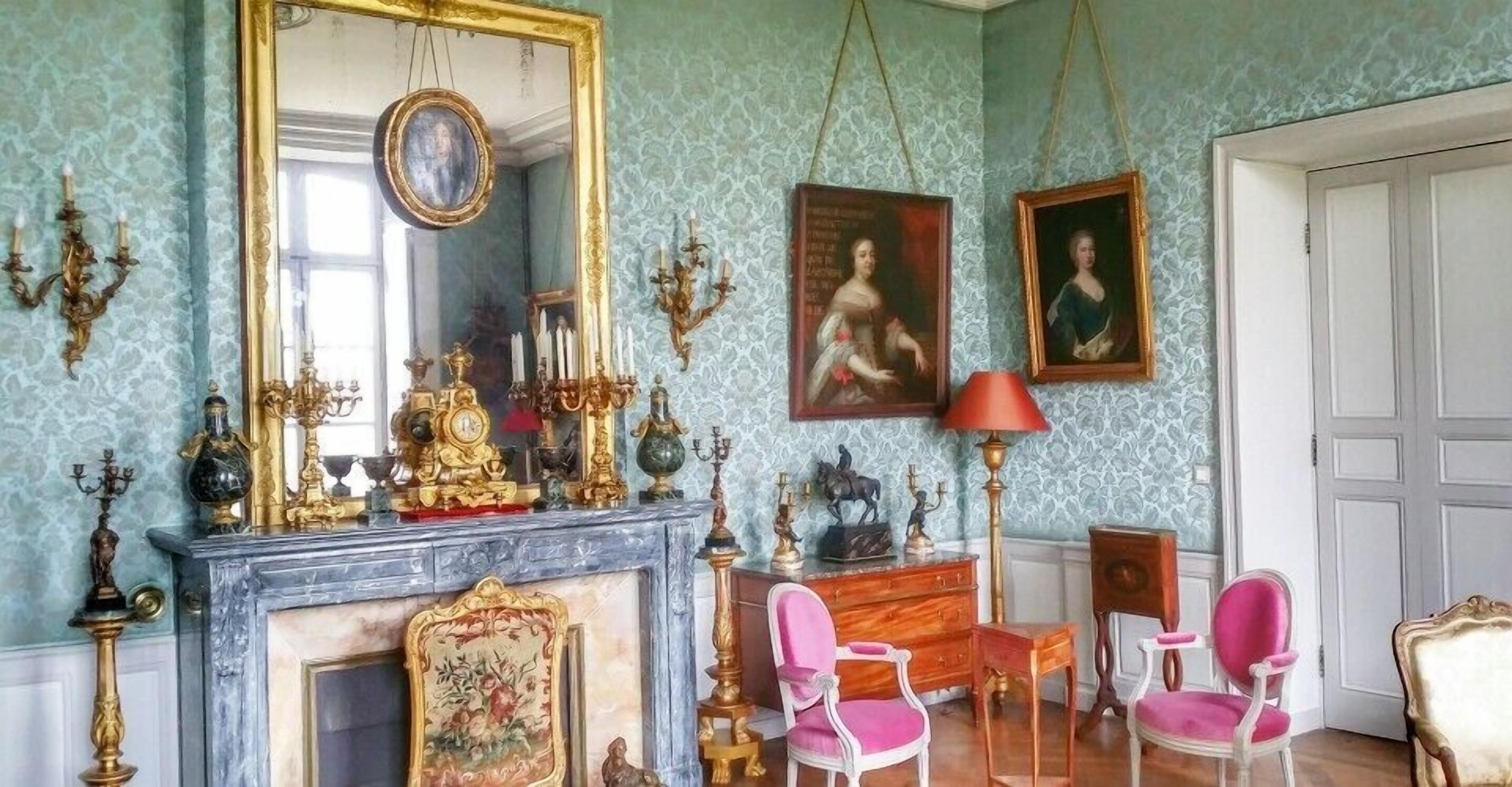 Een kamer met een marmeren open haard, een grote spiegel en twee ingekaderde portretten.