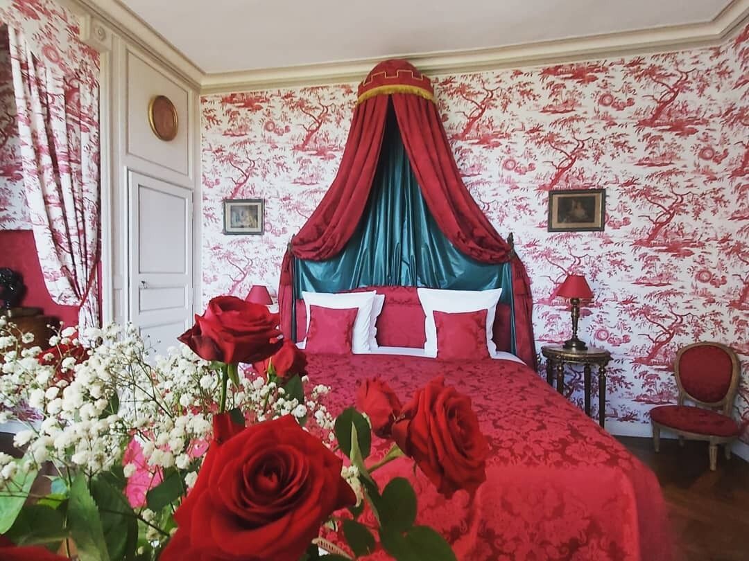 Et soveværelse med himmelseng, blomstret tapet og røde og hvide farver.