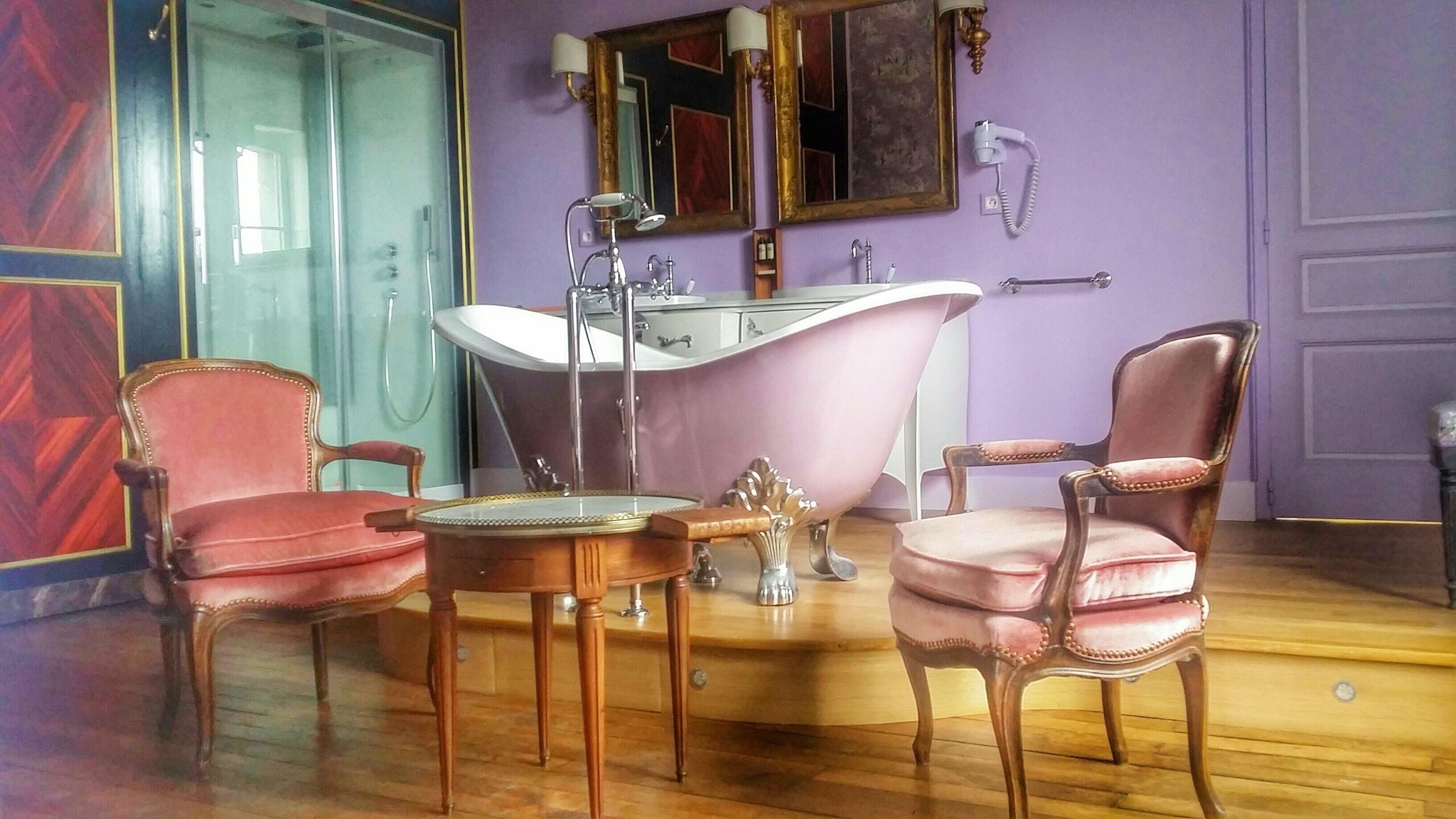 A bathroom with a freestanding bathtub, two antique chairs, a vanity with a mirror, and a shower area.