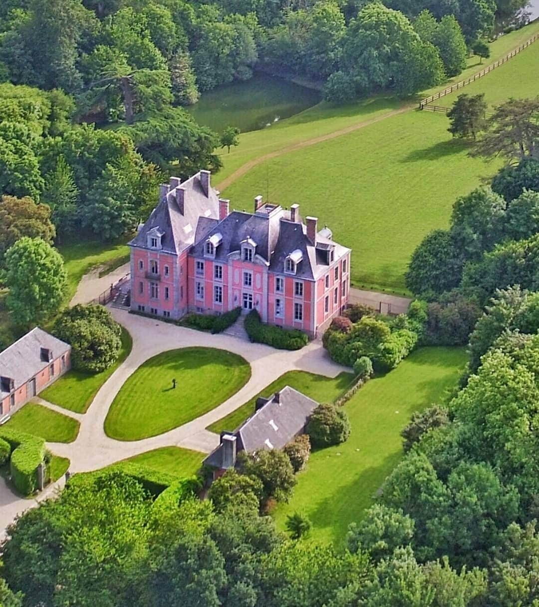 An aerial view of a large, pink, multi-story mansion with a symmetrical facade, surrounded by well-manicured lawns and a variety of trees.