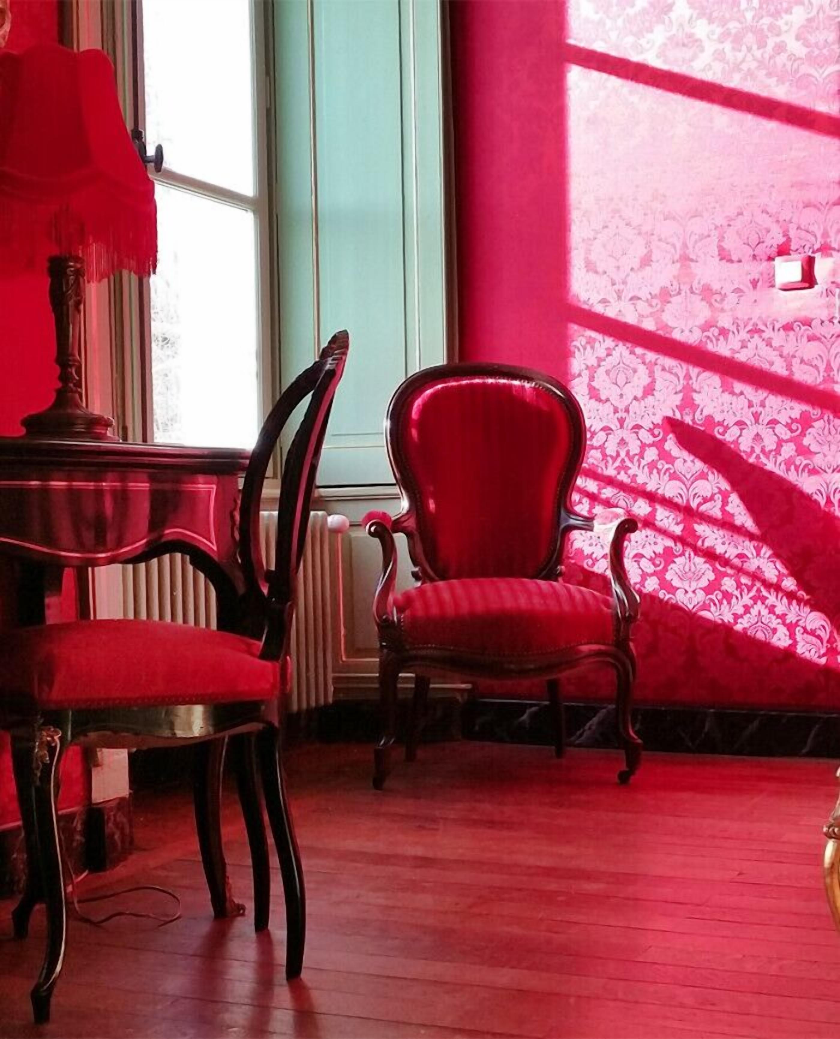 Una habitación con una silla roja, una mesa de madera y una ventana con vistas.
