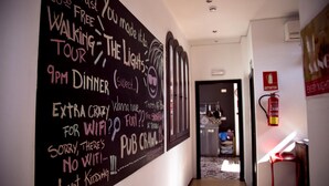 A hallway with a wall featuring a chalkboard with various messages and doodles, a fire extinguisher, and a red stool. - The Lights Hostel (Málaga)