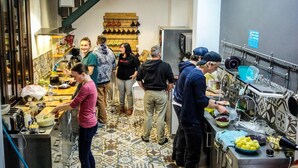 A busy kitchen with people preparing food, a staircase, and a variety of kitchen equipment. - The Lights Hostel (Málaga)