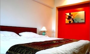 Ein Hotelzimmer mit einem Bett, einem Nachttisch mit Lampe und einer roten Akzentwand mit Gemälde.