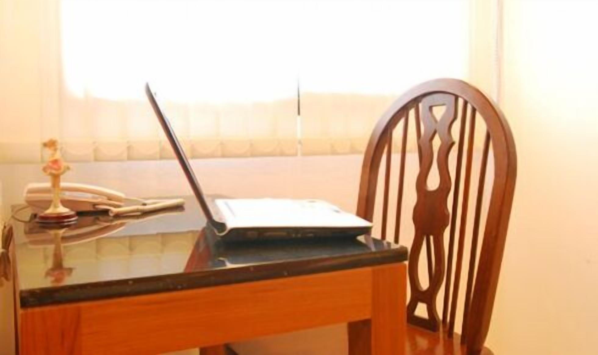 A laptop on a glass table with a decorative item and a telephone.