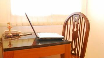 A laptop on a glass table with a decorative item and a telephone.