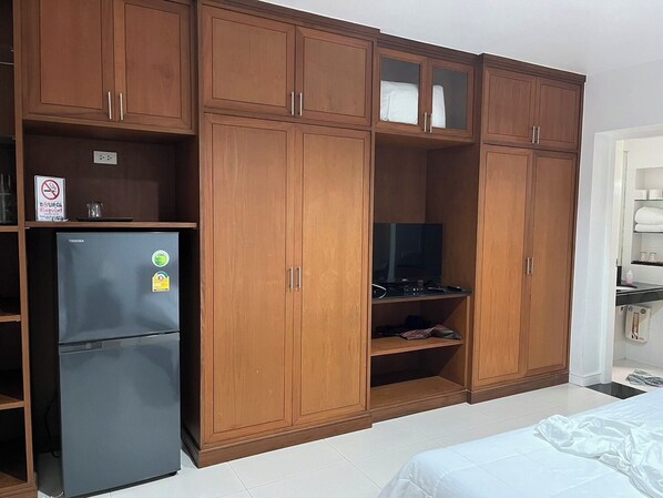Una habitación con armarios de madera, un refrigerador negro y una cama.