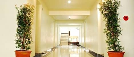 A hotel hallway with a polished floor, a staircase at the end, and potted plants on either side.