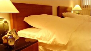Una habitación de hotel con cama, mesitas de noche, lámparas y un reloj.