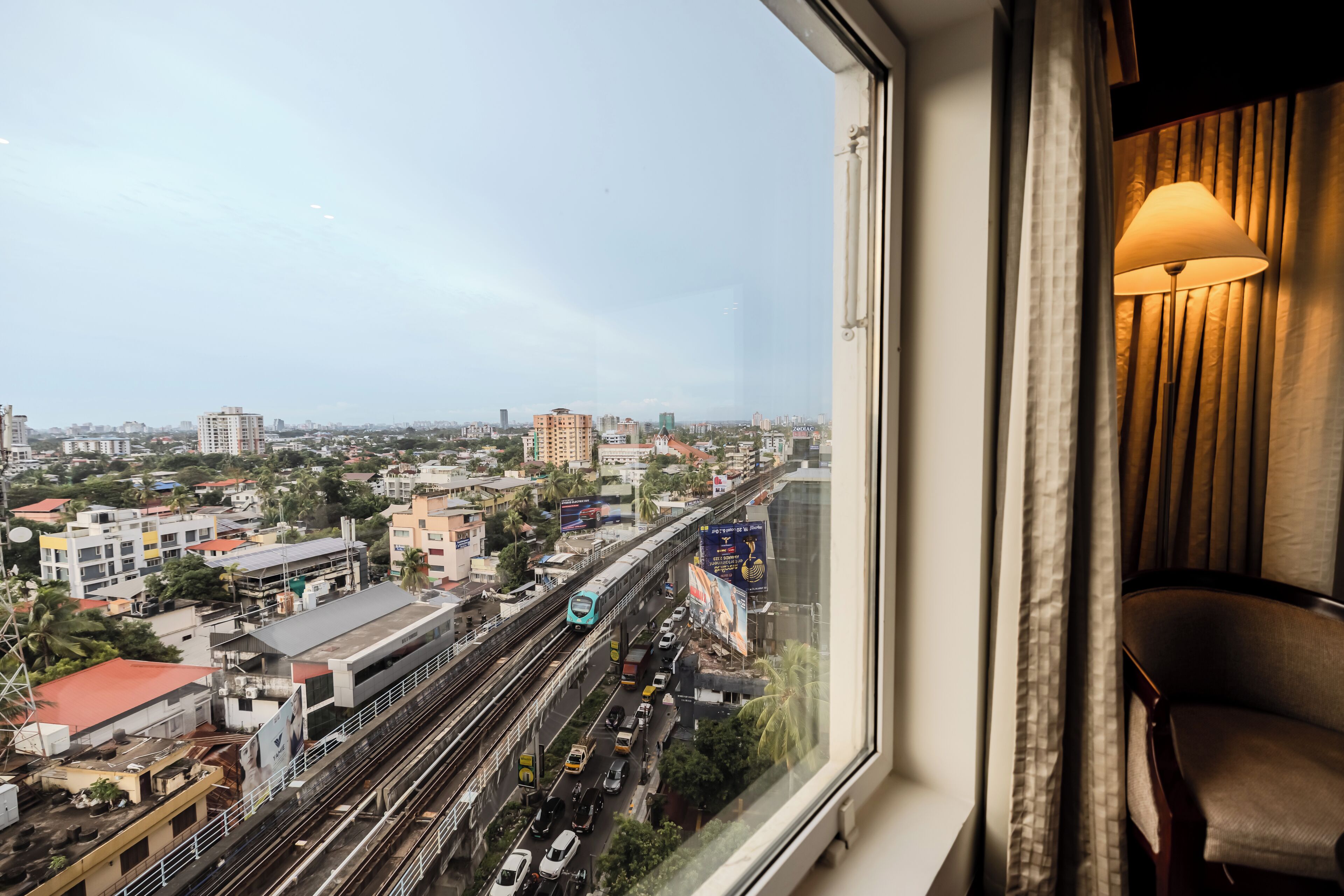 A room with a large window overlooking a busy cityscape, including a train track and various buildings.