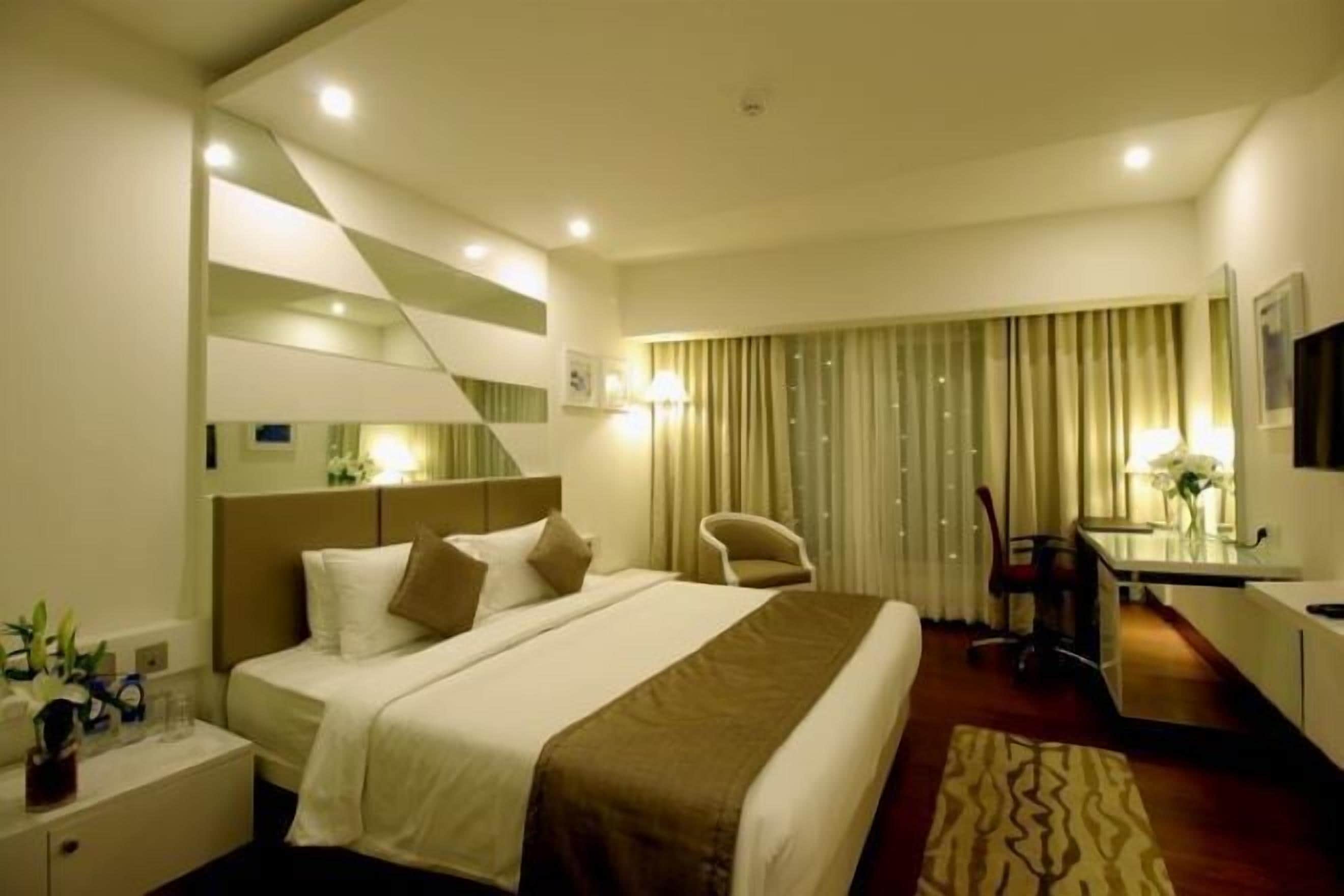 A hotel room with a bed, bedside table, lamp, chair, desk, and curtains.