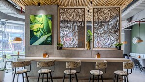 A modern bar area with a concrete counter, four bar stools, and decorative panels. - Olive Downtown Kochi (Kanayannur)