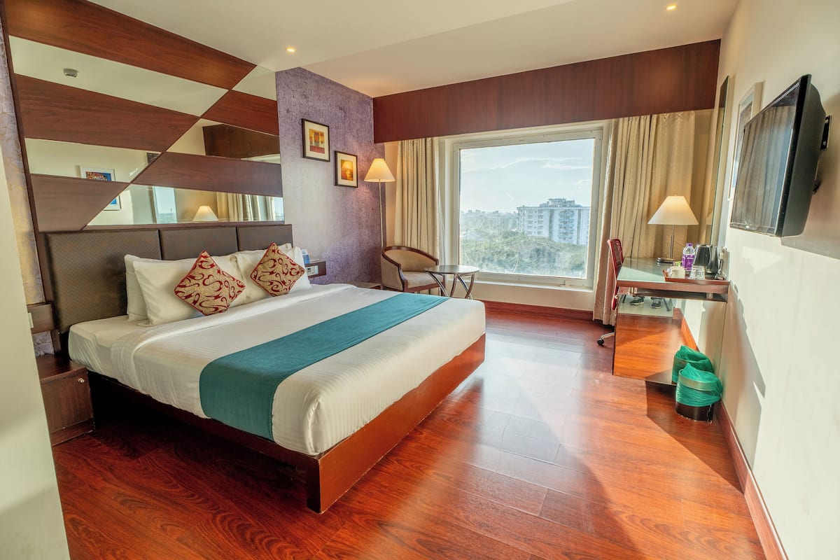 Una habitación de hotel con una cama grande, un escritorio con una silla, un televisor y una ventana con cortinas.