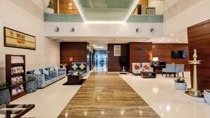 A spacious lobby with a marble floor, a seating area with sofas and armchairs, a reception desk, and a staircase leading to an upper level. - Olive Downtown Kochi (Kanayannur)