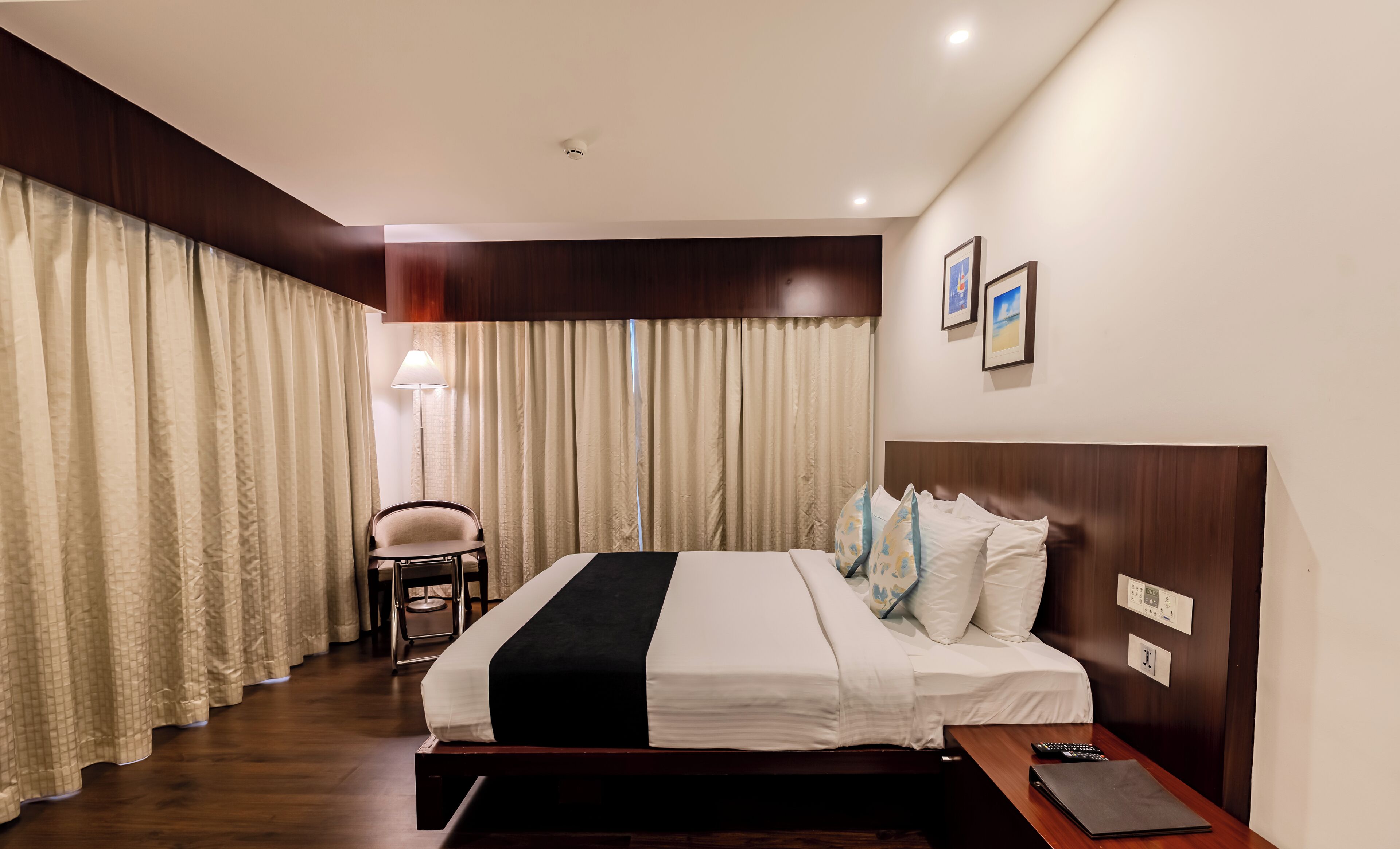 A hotel room with a large bed, a bedside table, a chair, and a lamp.