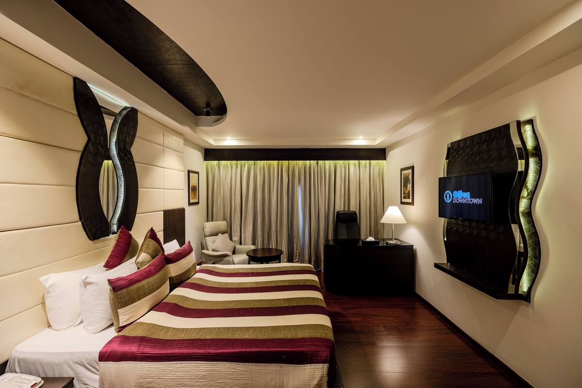 Habitación de hotel con una cama grande, televisión, escritorio, silla y ventana con cortinas.