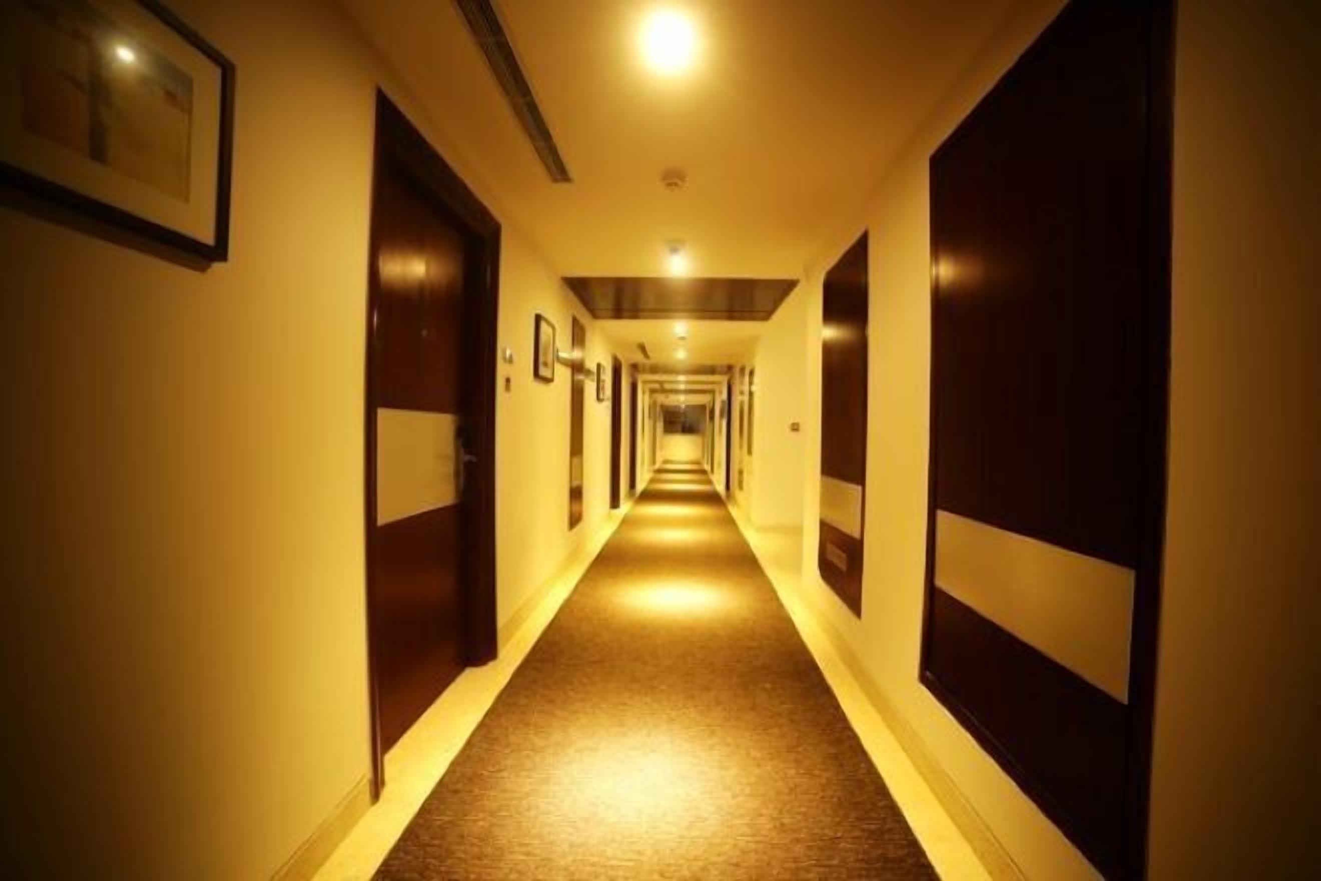 A long, narrow hotel corridor with doors on both sides, illuminated by overhead lighting.