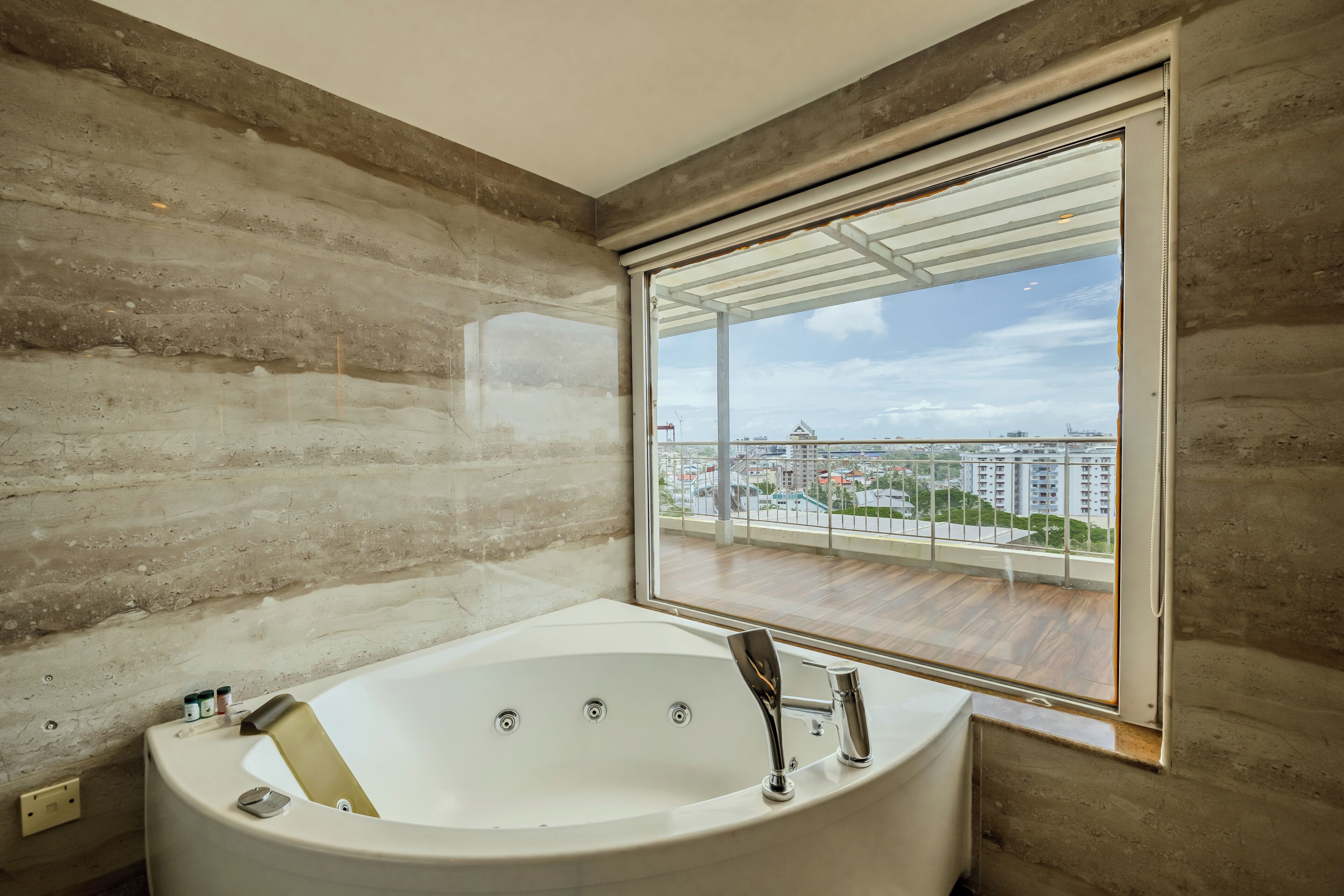 Ein modernes Badezimmer mit einer großen Badewanne, einem Fenster mit Blick auf eine Stadtlandschaft und einer Betonwand.