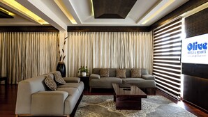 A modern living room with a sofa set, a coffee table, and a large TV screen displaying the hotel name. - Olive Downtown Kochi (Kanayannur)