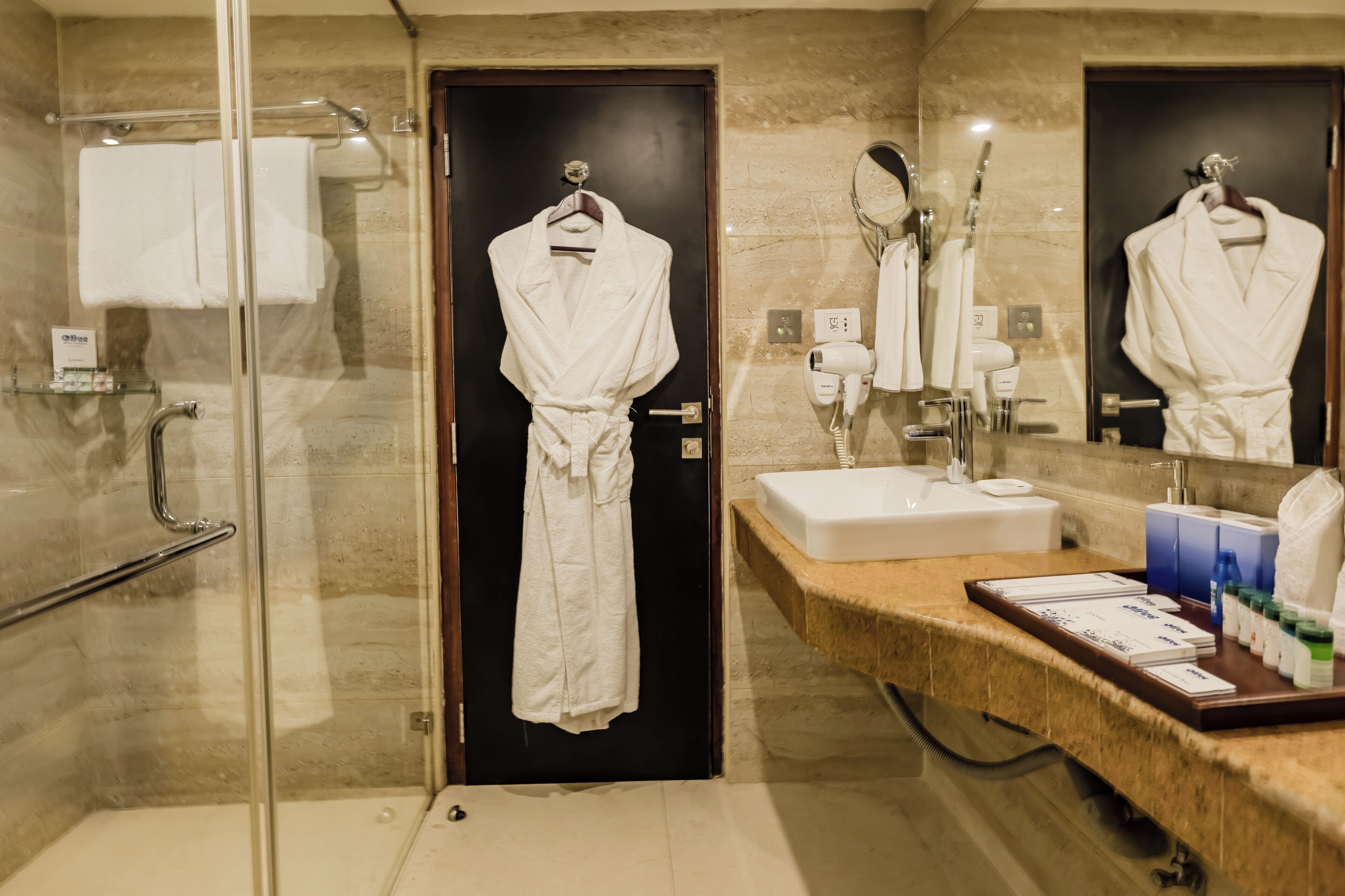 A modern bathroom with a glass shower enclosure, a sink with a vanity, and a robe hanging on a door.