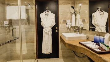 A modern bathroom with a glass shower enclosure, a sink with a vanity, and a robe hanging on a door.