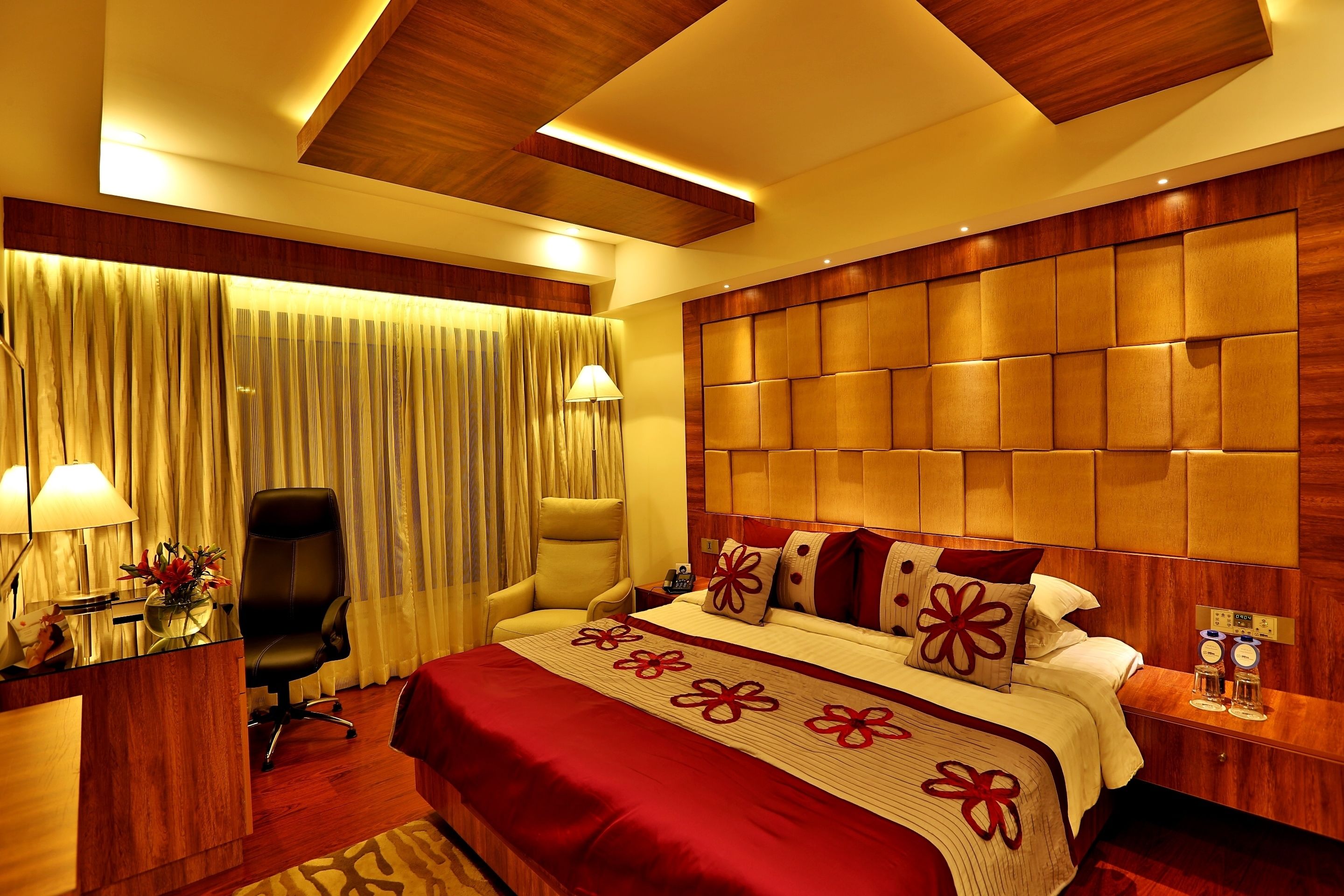A hotel room with a large bed, a desk, a chair, and a bedside table with a lamp.