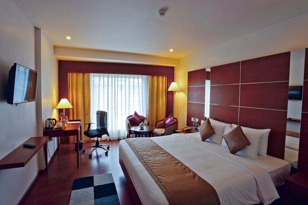 A hotel room with a large bed, a desk with a chair, a TV, and a window with curtains.
