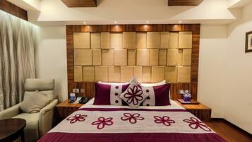 A hotel room with a large bed, a wooden headboard, a chair, a nightstand, and a bedside table.