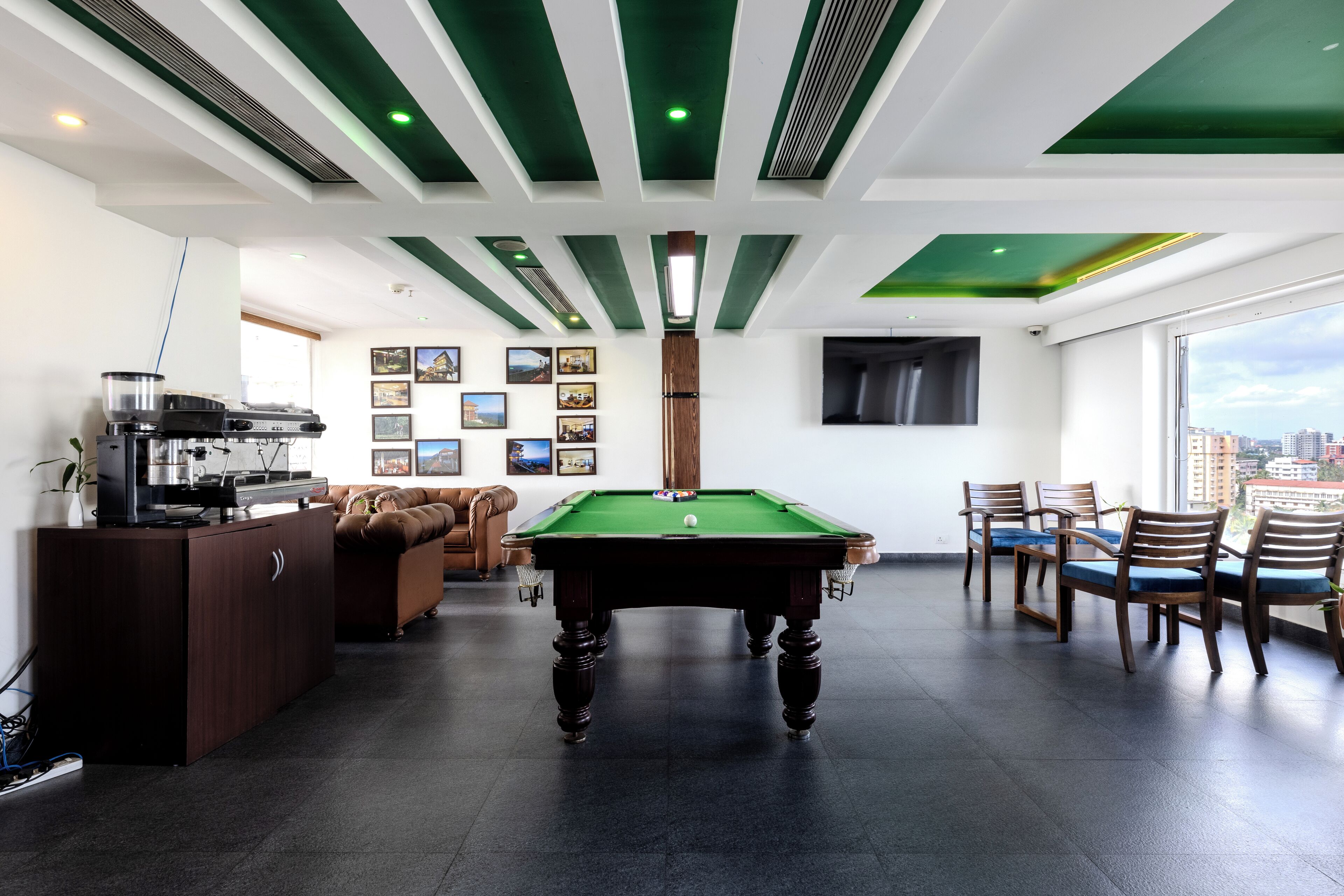 A pool table in a modern room with a green ceiling, a sofa, and a city view.