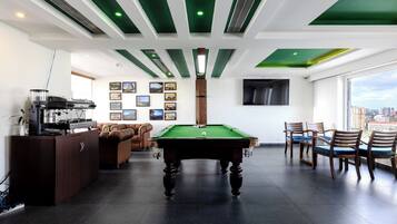 A pool table in a modern room with a green ceiling, a sofa, and a city view.