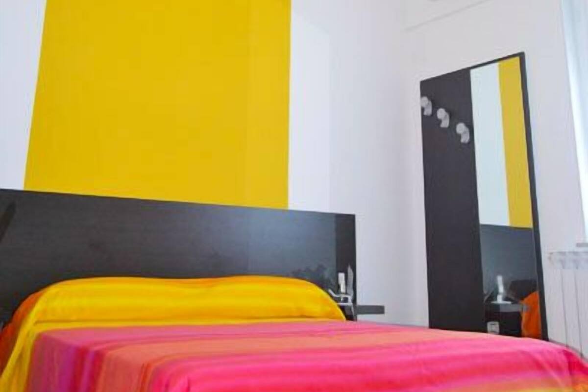 A modern hotel room with a large bed, a black headboard, and a bright yellow accent wall.