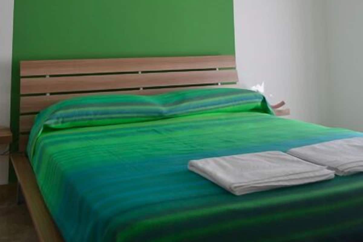 A room with a green wall, a wooden bed frame, and a green bedspread.