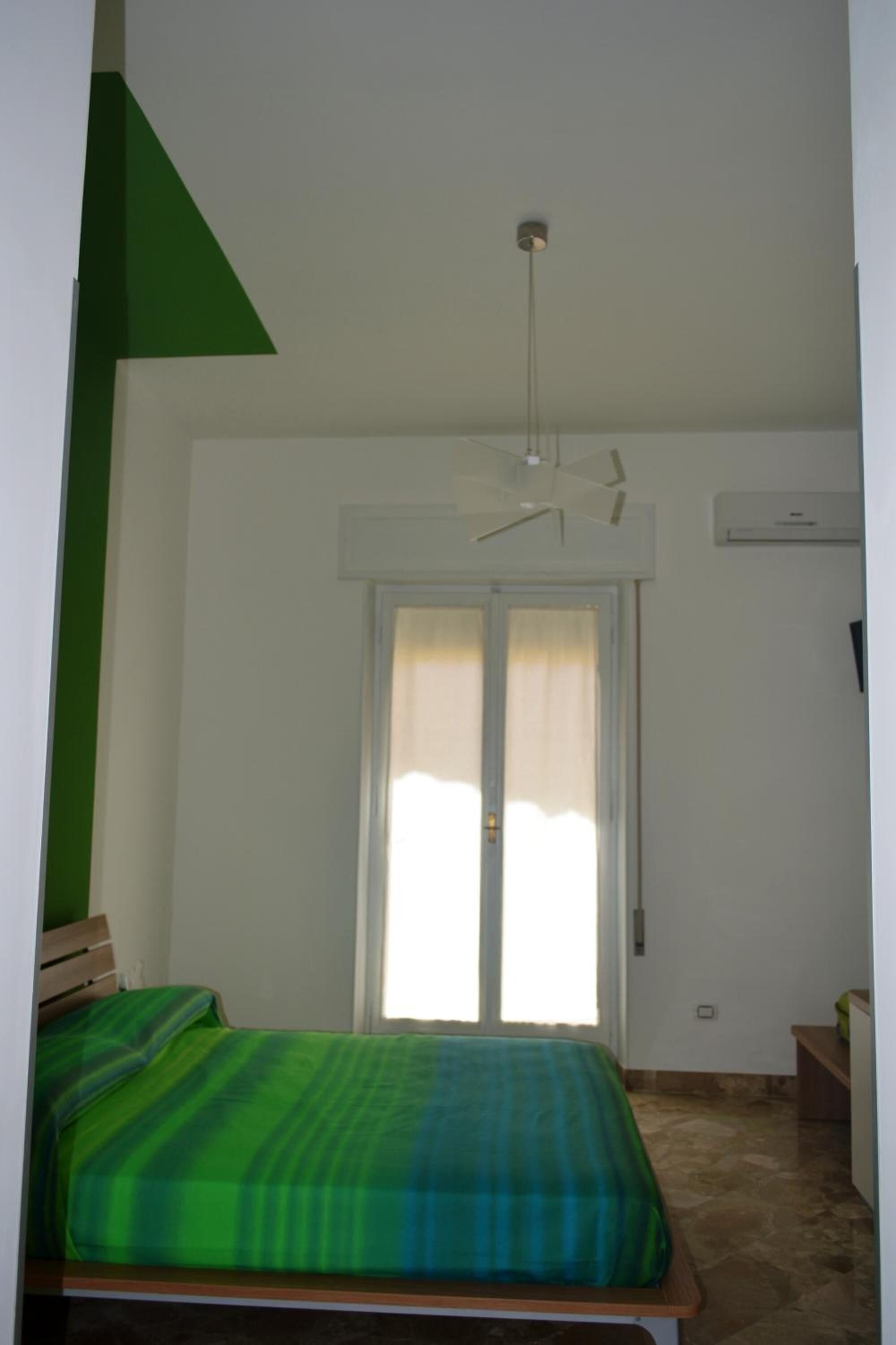 A bedroom with a bed, a ceiling fan, a window with curtains, and a door.