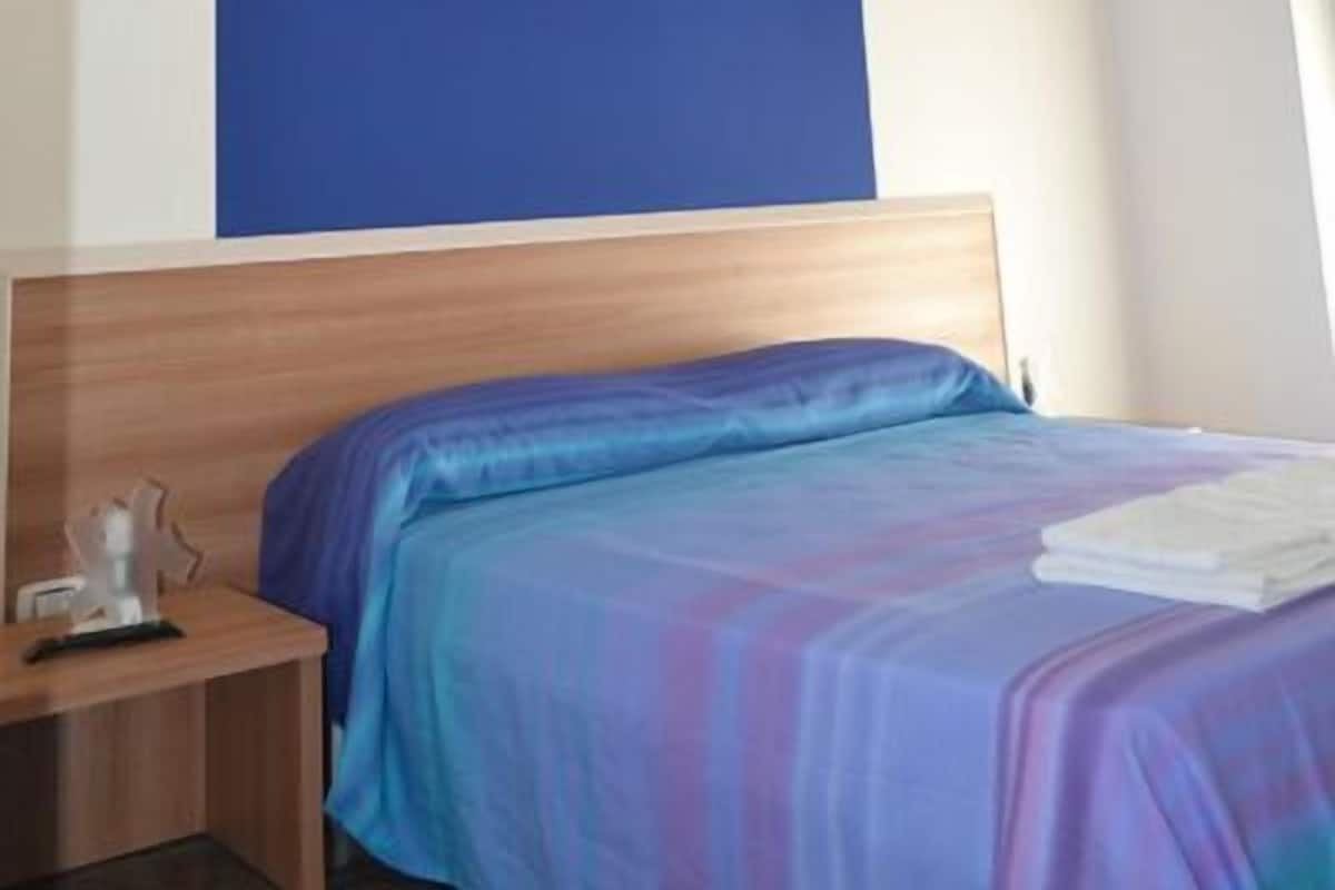 A hotel room with a bed, a wooden headboard, a nightstand, and a large blue accent wall.