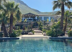 Un área de piscina con palmeras, un sendero de piedra y un edificio con montañas al fondo.