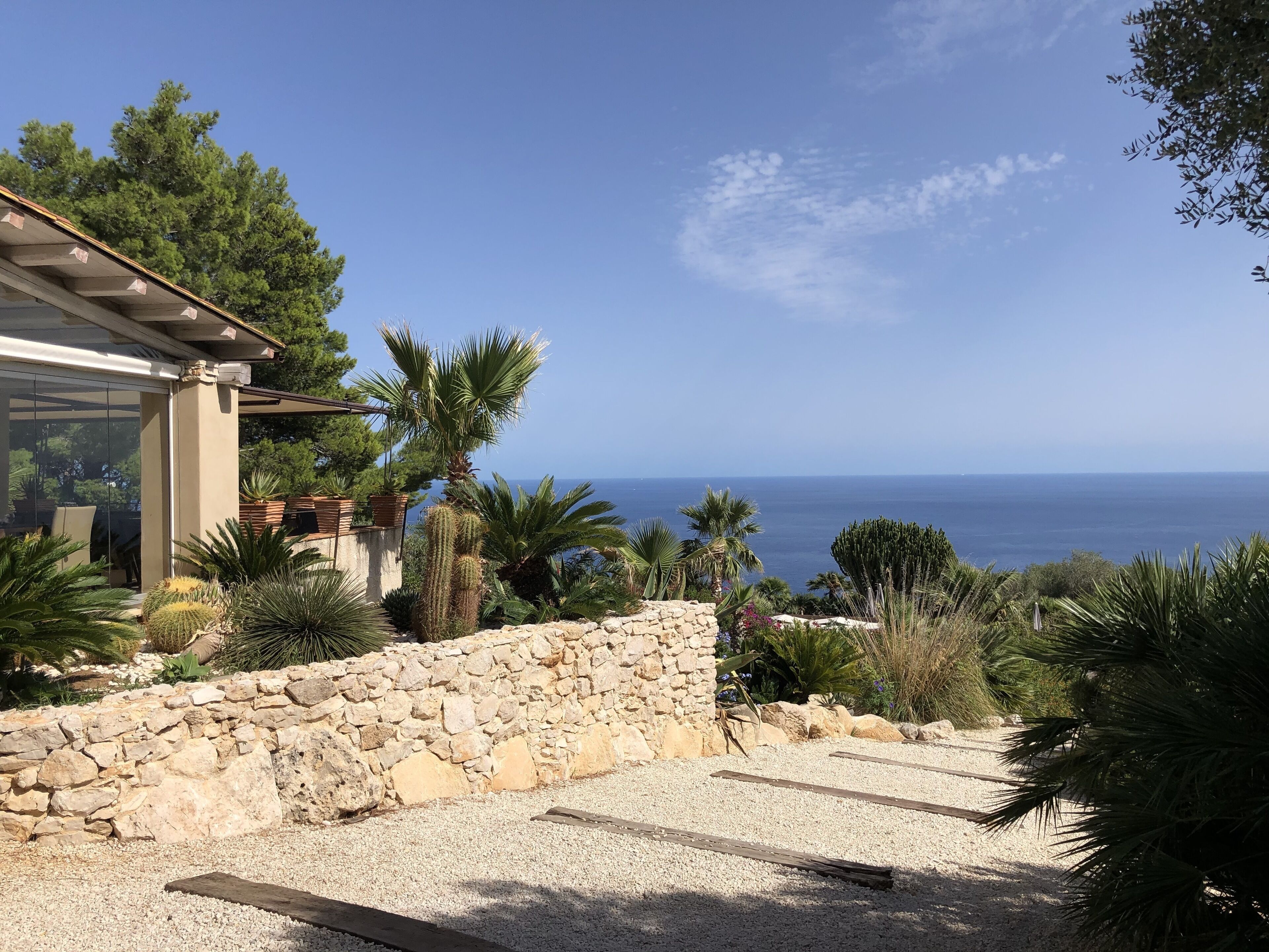 A coastal property with a stone wall, palm trees, and a view of the sea.
