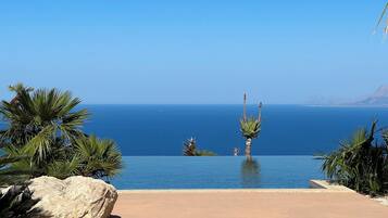 Vista despejada del océano desde la piscina infinita del resort, con palmeras y una roca grande al frente.
