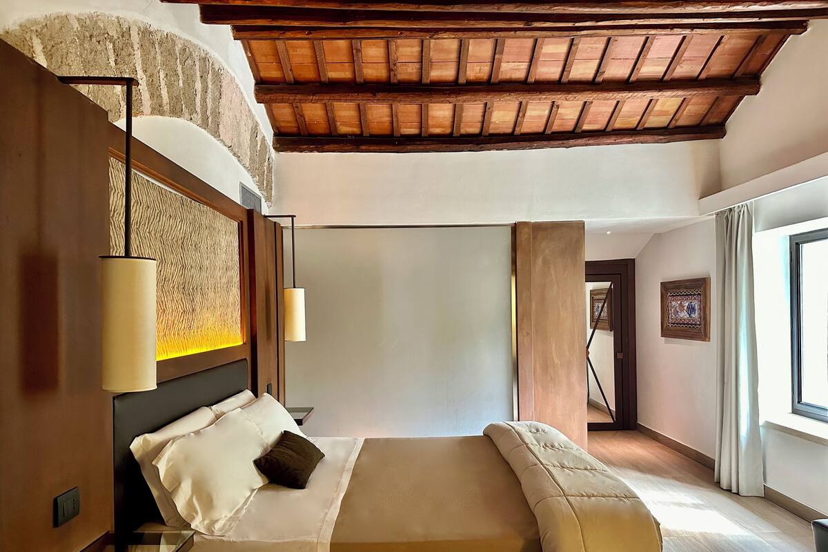 A hotel room with a bed, a nightstand, a lamp, a wall with a textured pattern, and a wooden ceiling.