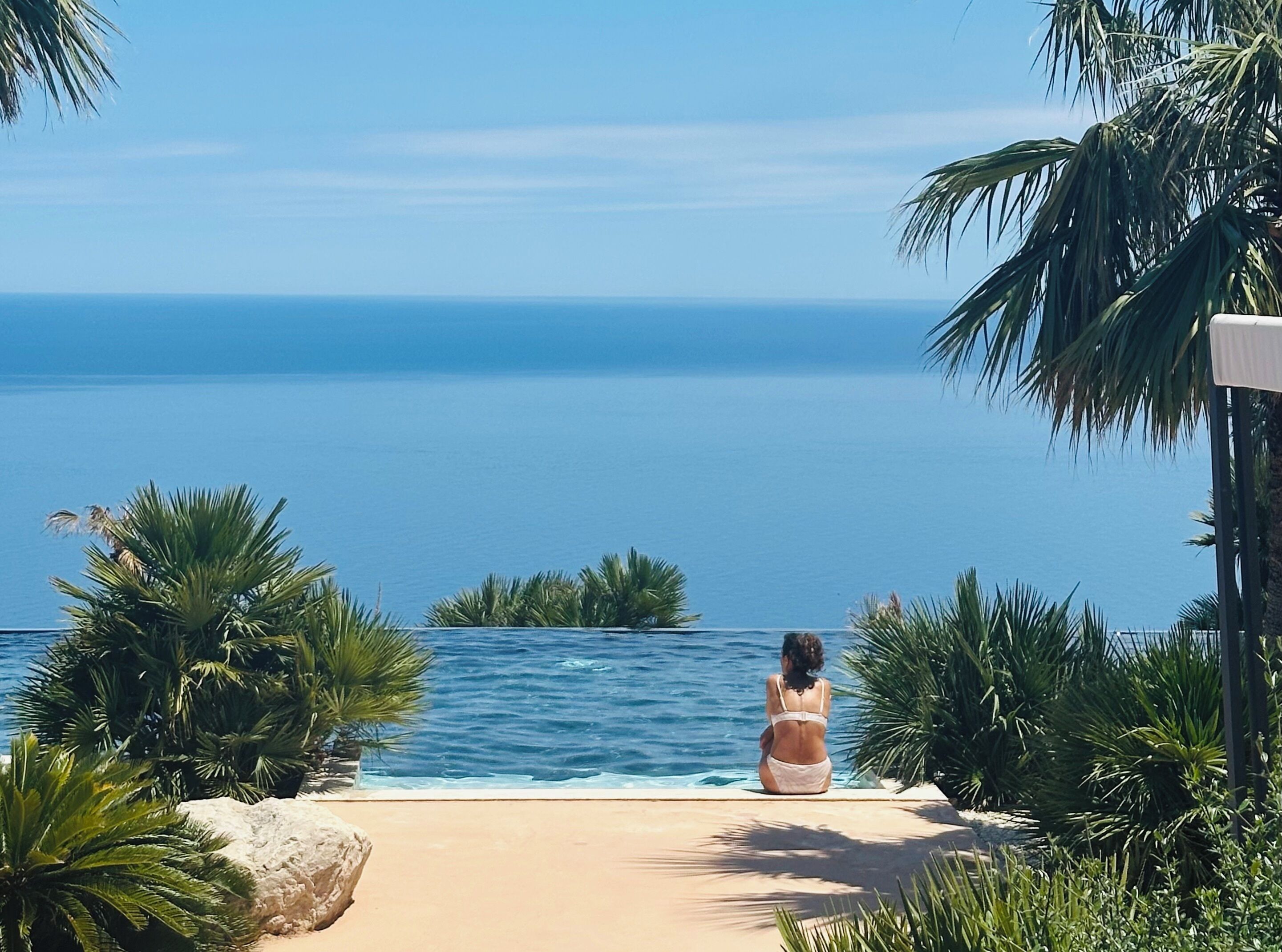Una persona sentada junto a una piscina con vista al océano.