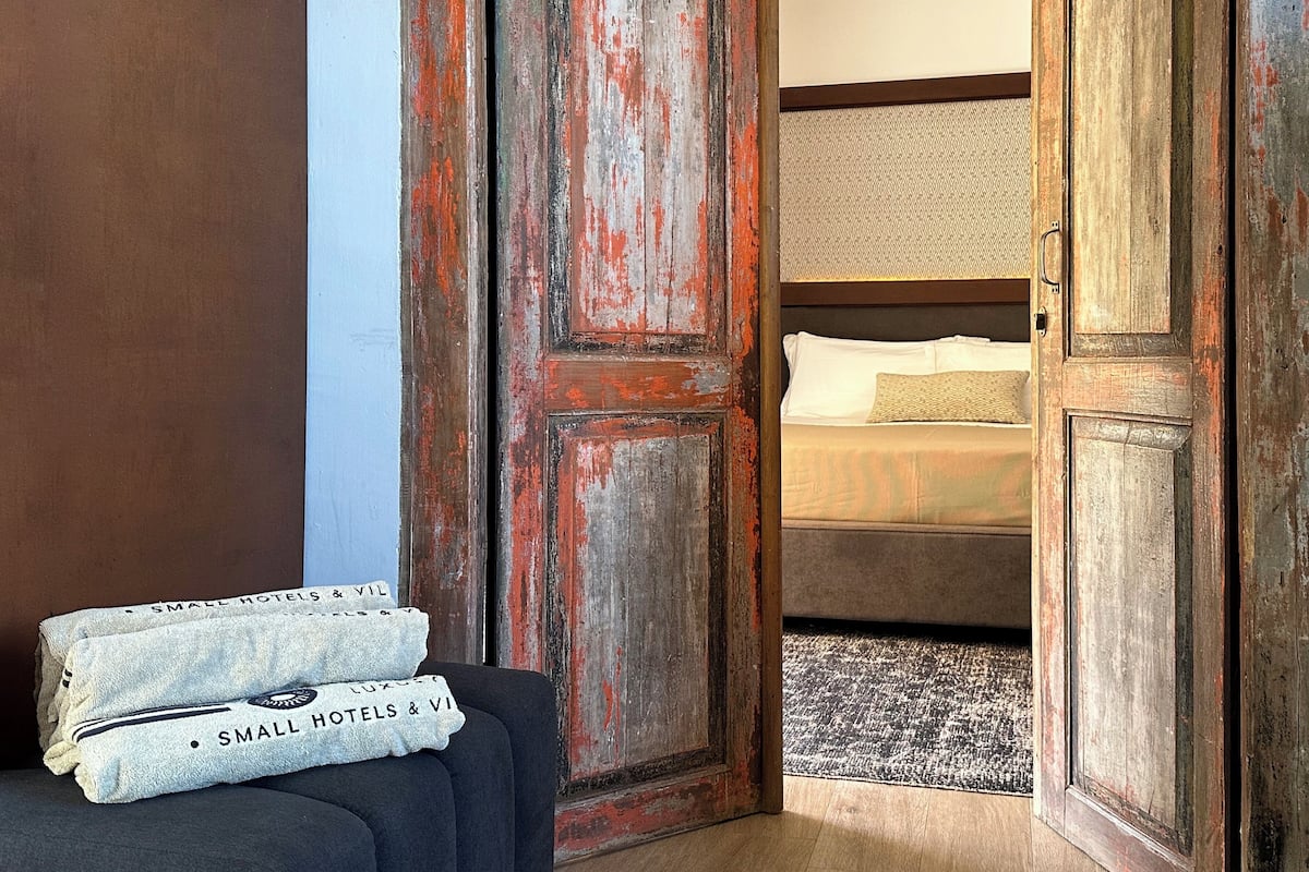 A room with a rustic wooden door, a bed with white bedding, and two towels with text on them.