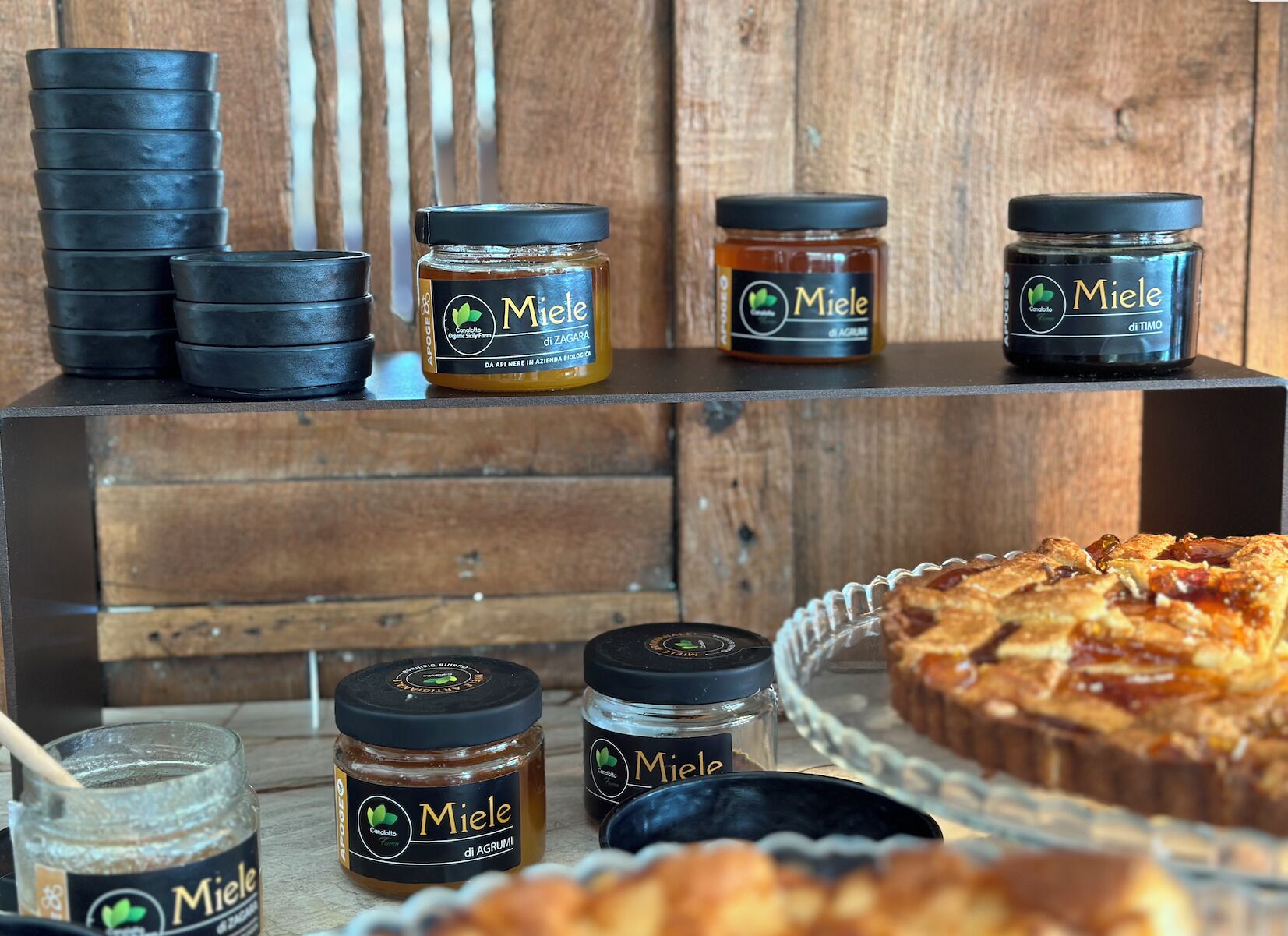 Una vitrina de madera con tarros de miel Miele y una bandeja de productos horneados.