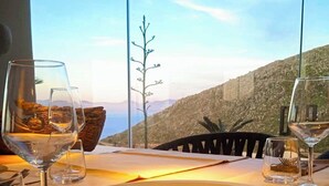 Une table avec une assiette de nourriture, deux verres à vin et une vue sur un paysage montagneux.