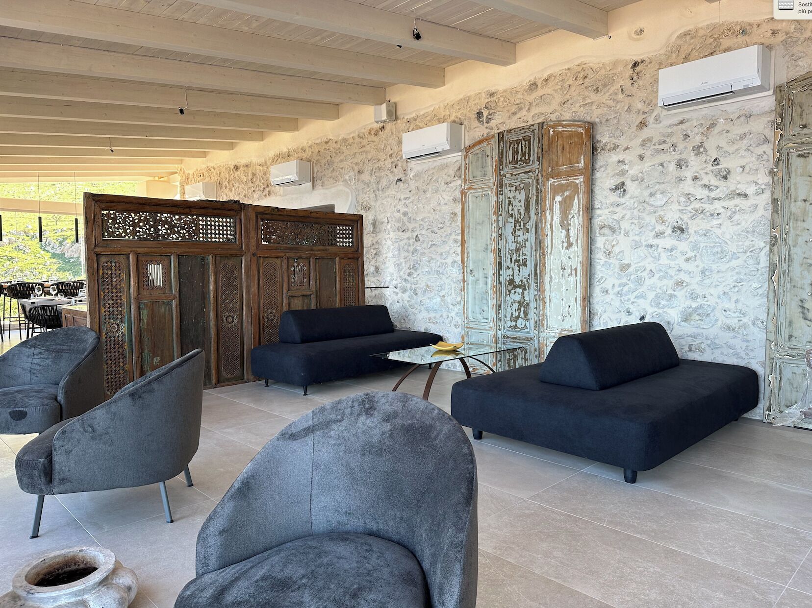 A modern lounge area with grey sofas and chairs, a decorative wooden partition, and a stone wall with an air conditioning unit.