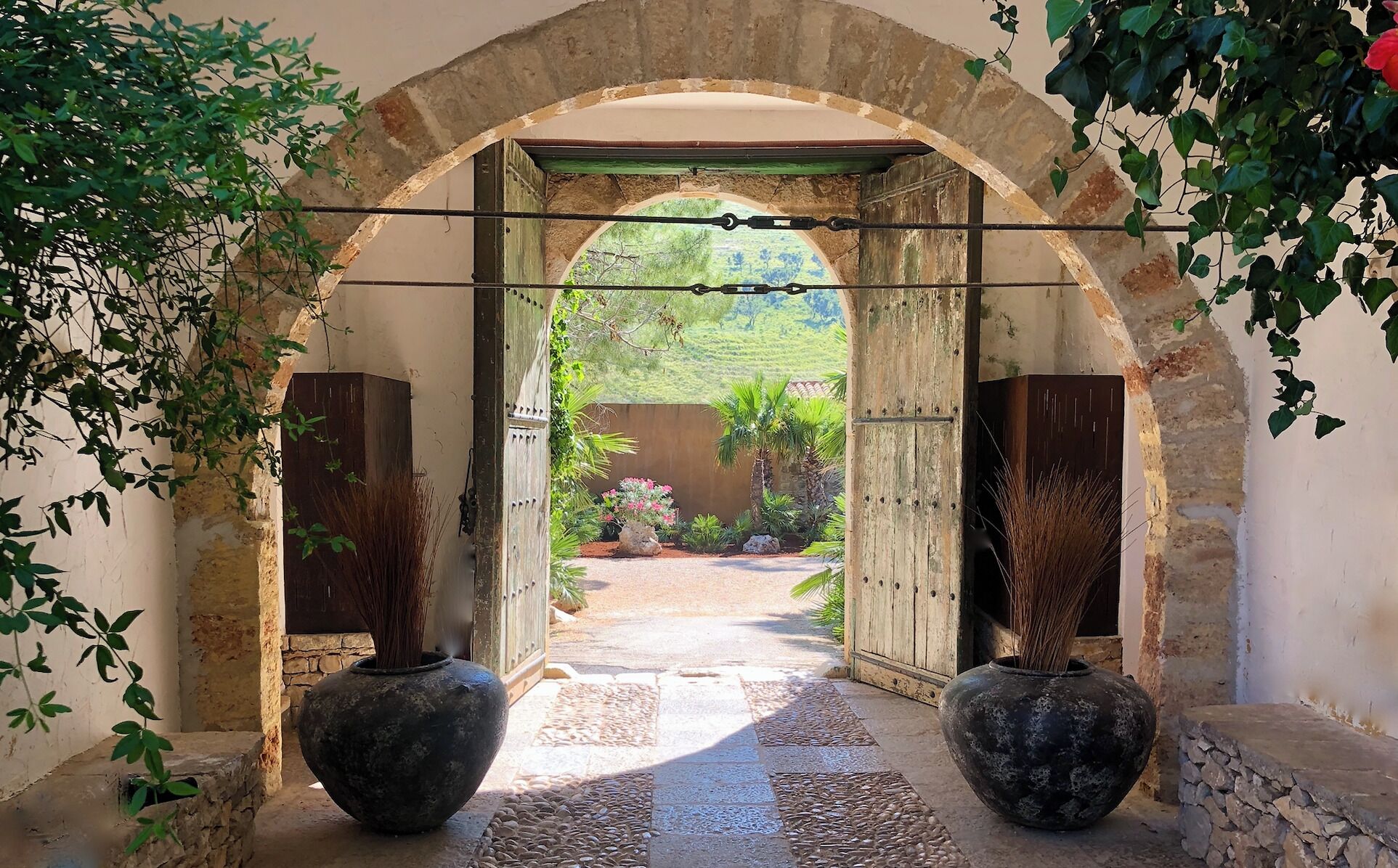 Una entrada arqueada con dos grandes jarrones a cada lado, que da a un jardín con vistas a la vegetación.