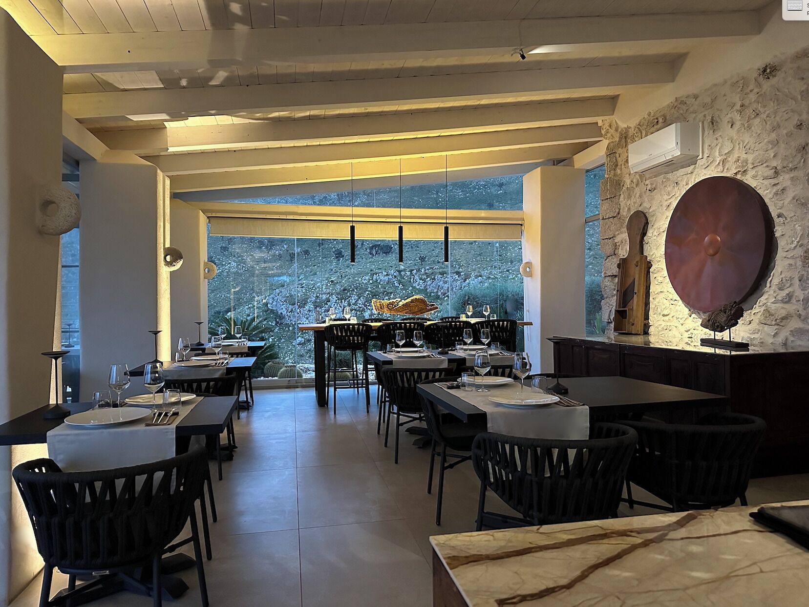 A modern dining area with tables and chairs, large windows, and a stone wall with a decorative plate.